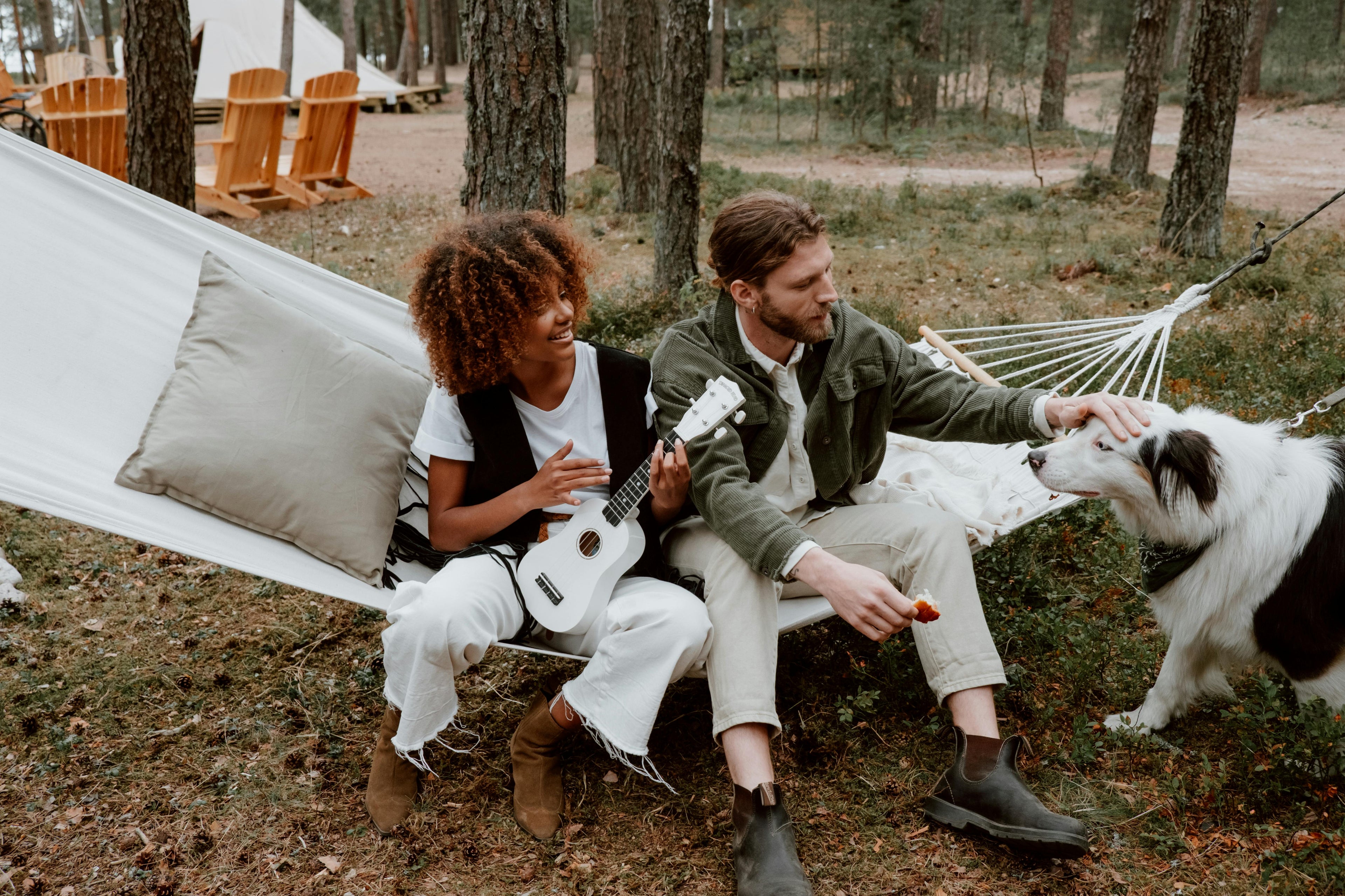 Two people sitting in a hammock with a dog in a forest setting